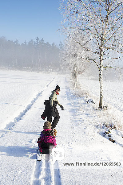 A mother pulling her two young daughters on a sled