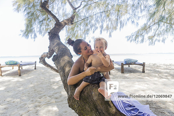 Kleinkind und seine Mutter sitzen auf einem Baum am Diani Beach Kenia