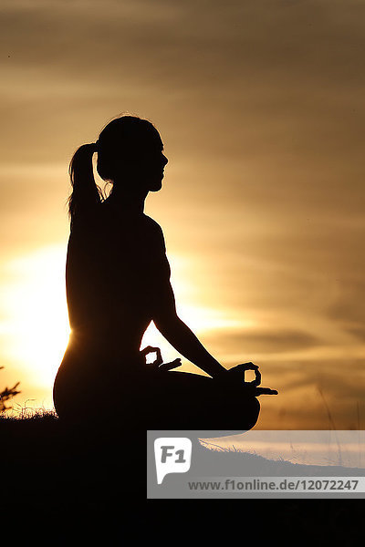 Silhouette einer Frau  die im Licht der Abendsonne Yoga übt. Lotus-Stellung. Französische Alpen. Frankreich.