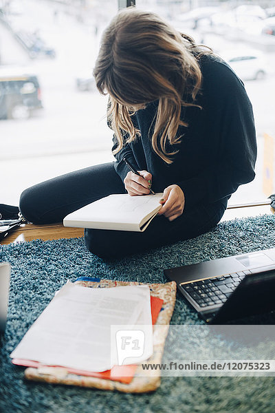Großer Blickwinkel auf die Geschäftsfrau beim Schreiben auf dem Notizblock in der Bürocafeteria