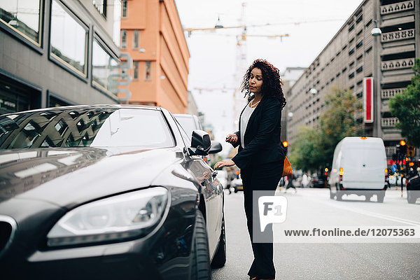 Full length of mid adult businesswoman standing by car on street in city