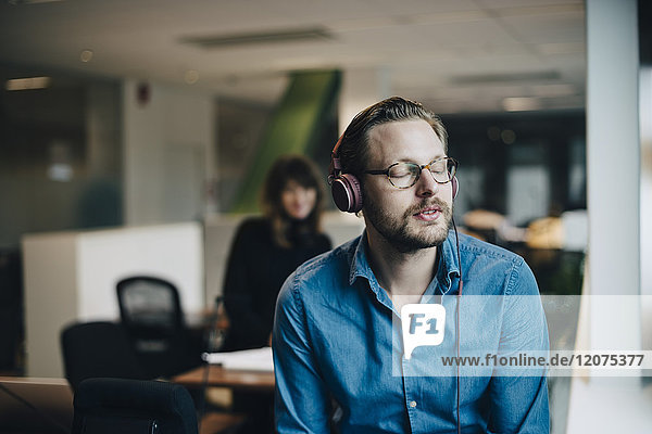 Mid adult businessman listening to headphones with eyes closed at office