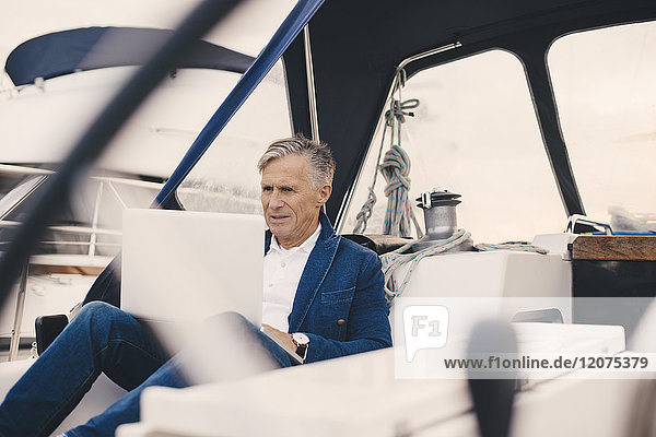 Senior man using laptop while sitting in yacht during vacation