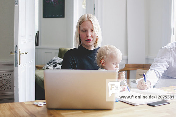 Businesswoman with baby girl using laptop at table in creative office