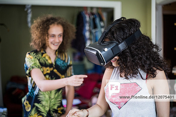 Smiling teenage boy pointing at girl wearing virtual reality headset at home