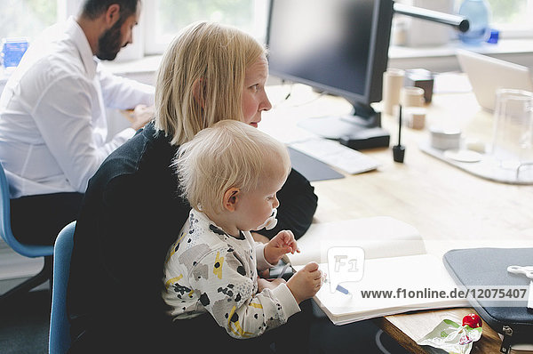 Businesswoman with daughter writing in book at table in creative office