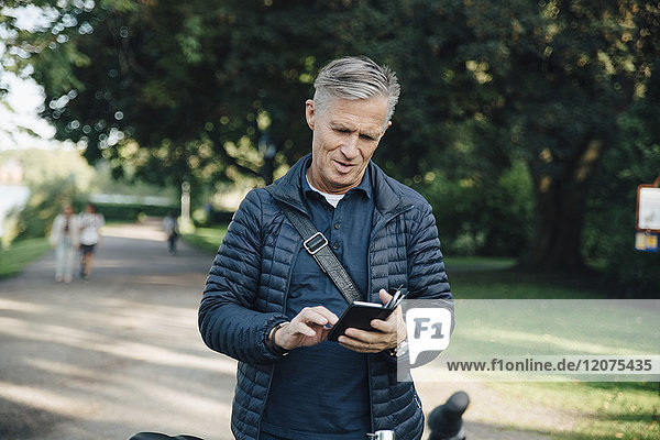 Senioren-Mann  der im Park steht und sein Handy benutzt