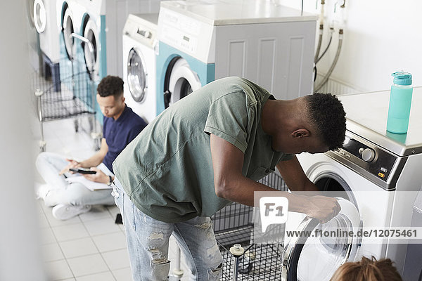 Mann mit Waschmaschine während des Studiums am Waschsalon