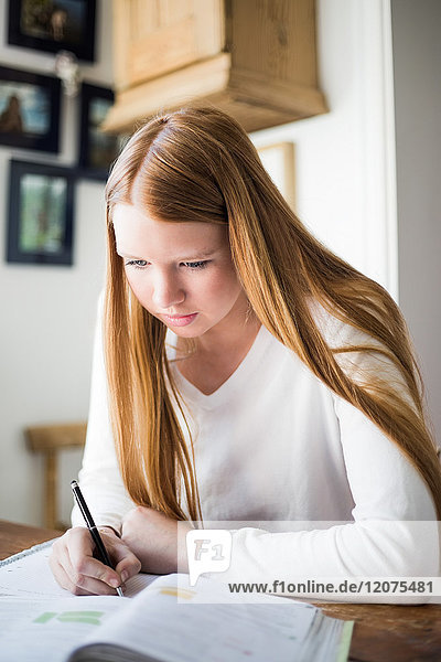 Blond girl studying at table while writing in book