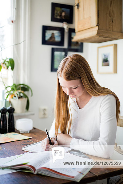 Blond girl writing in book while sitting at home