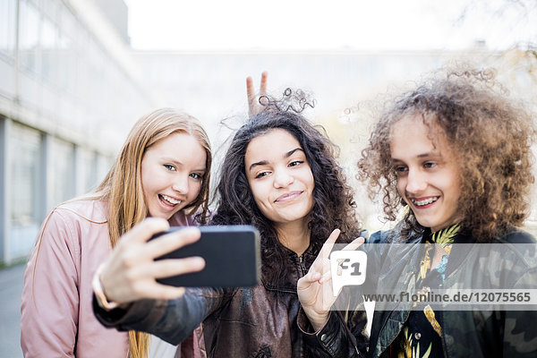 Lächelndes Teenager-Mädchen nimmt Selfie mit Freunden von Smartphone