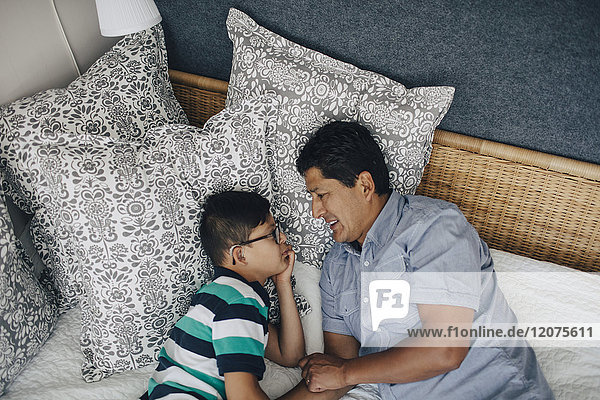 High angle view of father talking to son while lying on bed at home