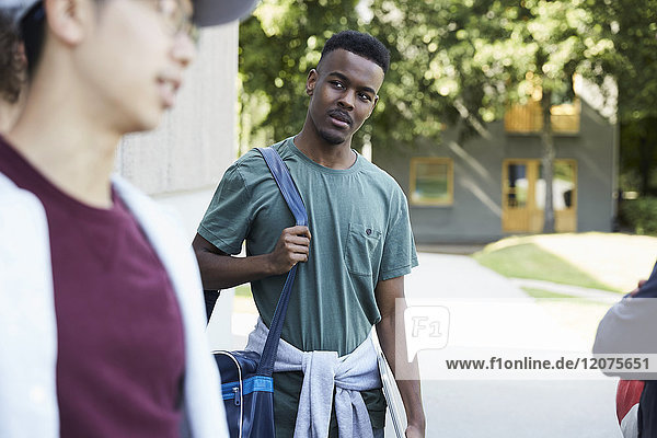 Thoughtful man carrying shoulder bag while walking with friends at university campus