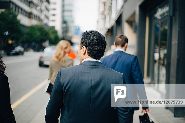 Rear view of businessman walking behind colleagues on sidewalk in city