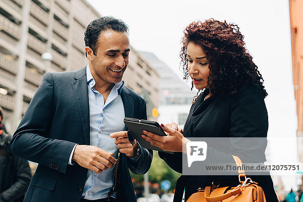 Low angle view of businesswoman discussing over digital tablet to businessman while standing on sidewalk in city