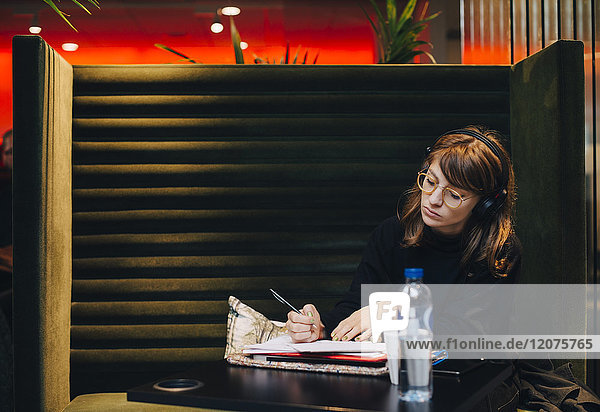 Junge Geschäftsfrau schreibt im Tagebuch  während sie in der Cafeteria sitzt.