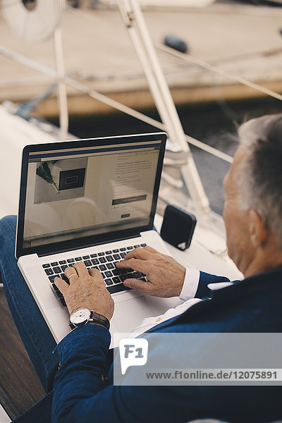 Hochwinkelansicht des älteren Mannes  der den Laptop benutzt  während er auf der Yacht sitzt.