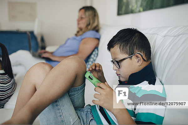 Behinderter Junge mit digitalem Tablett und Mutter mit Laptop auf dem Sofa