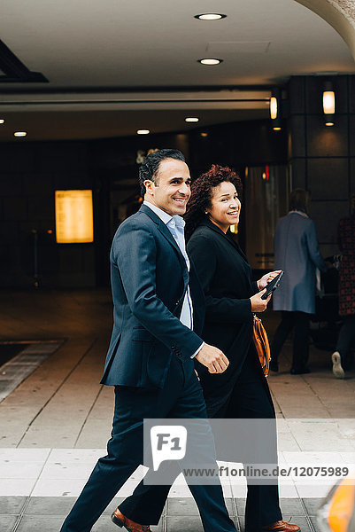 Side view of smiling business colleagues walking on sidewalk in city
