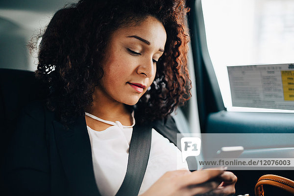 Mittlere erwachsene Geschäftsfrau beim Sitzen mit dem Smartphone im Taxi