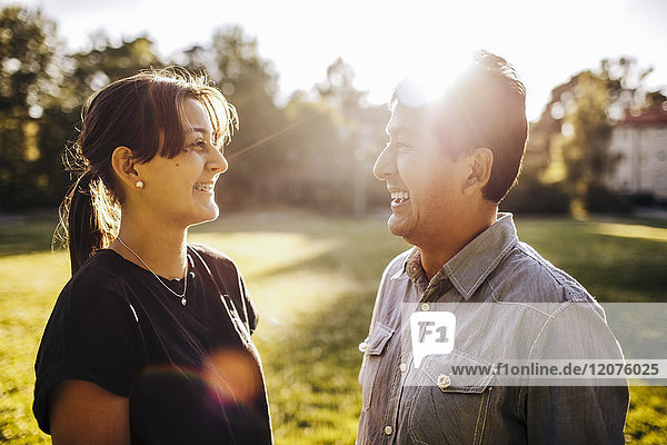 Close-up of smiling father and daughter talking while standing on grassy field at park during sunny day