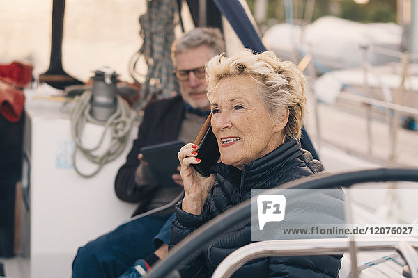 Seniorin spricht auf dem Handy  während sie von einem Mann auf einer Yacht sitzt.