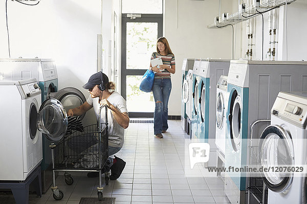 Mann mit Waschmaschine  während Frau im Waschsalon läuft