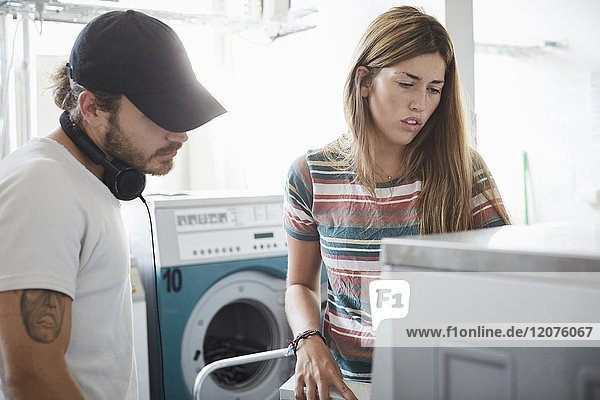 Mann hilft der Freundin bei der Benutzung der Waschmaschine im Waschsalon während des sonnigen Tages.