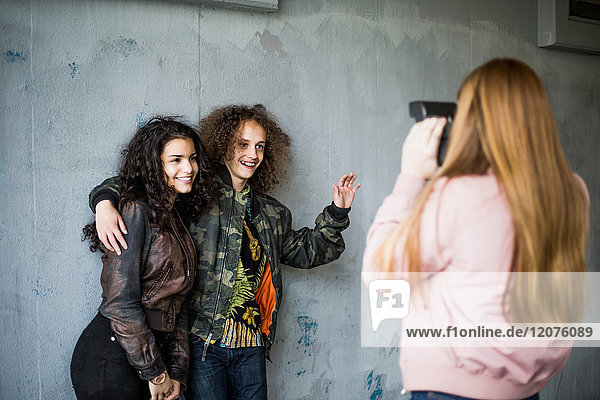 Rear view of girl photographing smiling teenage friends standing against wall at parking garage