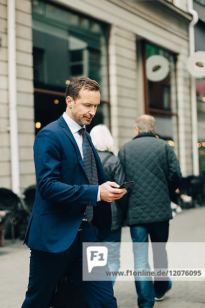 Reife Geschäftsleute mit Smartphone beim Gehen auf dem Bürgersteig in der Stadt