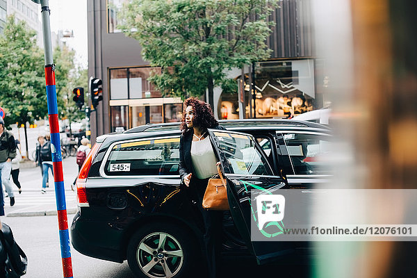 Mittlere erwachsene Geschäftsfrau beim Aussteigen aus dem Taxi auf der Straße in der Stadt