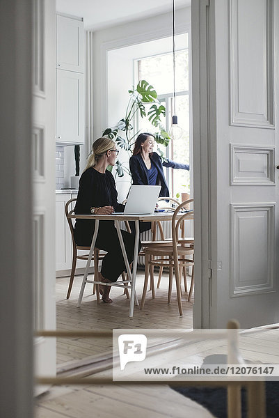 Female colleagues by table seen through doorway at home