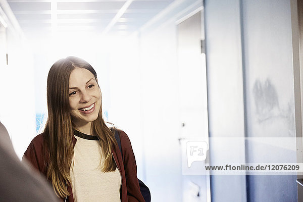 Lächelnder Student schaut weg während er im Flur der Universität steht.