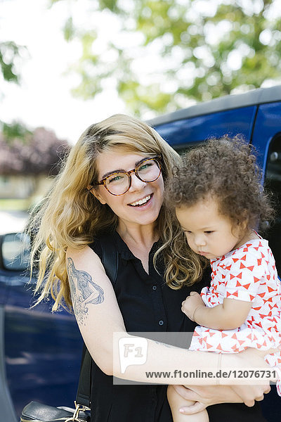 Mutter trägt Tochter (12-17 Monate) vor ein Auto