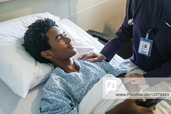 Arzt tröstet Jungen im Krankenhausbett mit Handy in der Hand