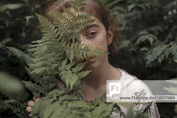Pensive Caucasian girl behind green leaves