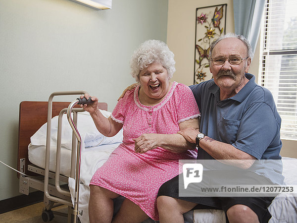 Kaukasischer Mann sitzt auf dem Bett und umarmt eine lachende Frau