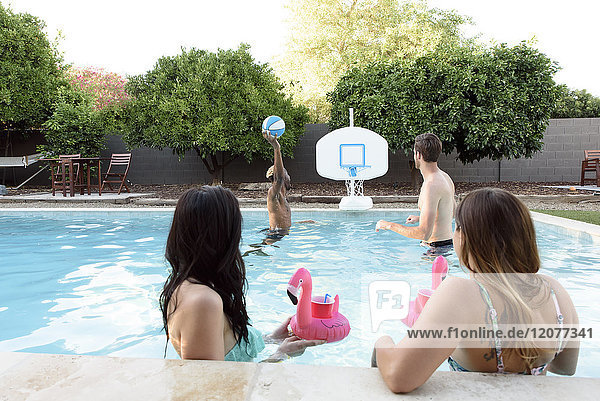 Frauen schauen Männern beim Basketballspielen im Schwimmbad zu