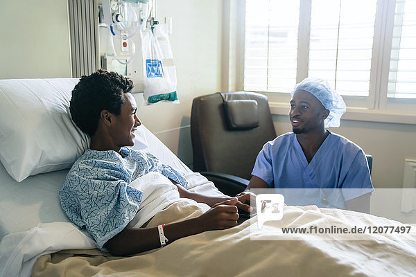 Schwarze Krankenschwester im Gespräch mit einem Jungen im Krankenhausbett