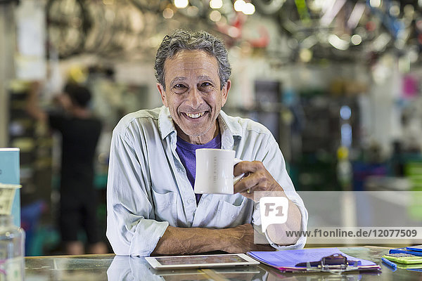 Porträt eines lächelnden kaukasischen Mannes  der in einem Fahrradgeschäft Kaffee trinkt