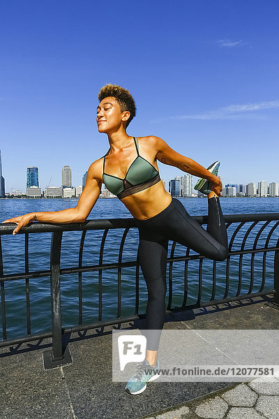 Mixed race woman stretching legs at waterfront