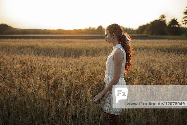 Pensive Caucasian girl standing in field of wheat