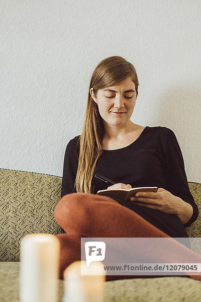 Smiling woman sitting on couch writing in notebook