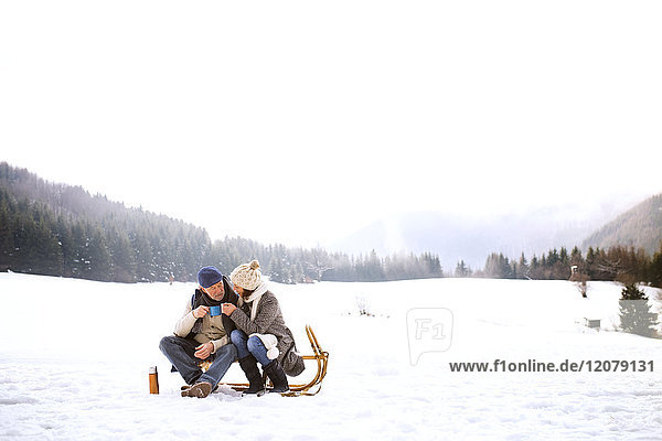 Seniorenpaar sitzend nebeneinander auf Schlitten in verschneiter Landschaft