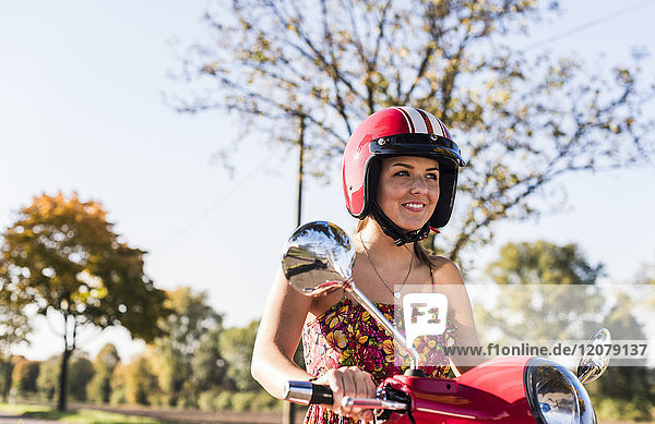 Porträt der lächelnden jungen Frau auf dem Motorroller