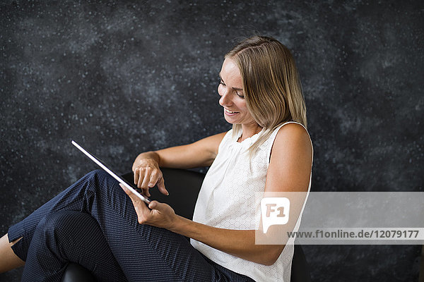 Lächelnde Geschäftsfrau im Sessel sitzend mit Tablette