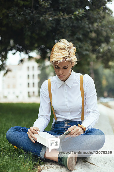Teenage girl sitting cross-legged in a park  reading book