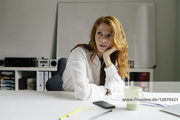 Junge Frau mit Tasse Kaffee am Schreibtisch im Büro