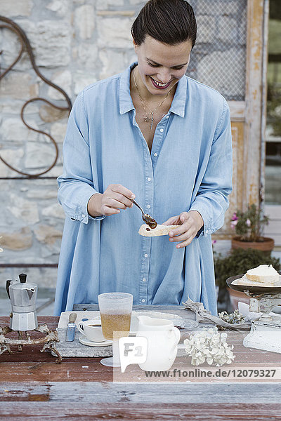 Italien  lachende Frau  die Marmelade auf eine Brotscheibe auf der Terrasse legt.