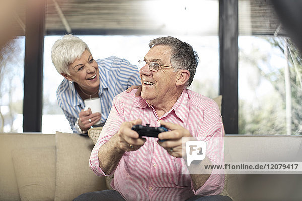 Happy senior man with wife playing video game on couch at home